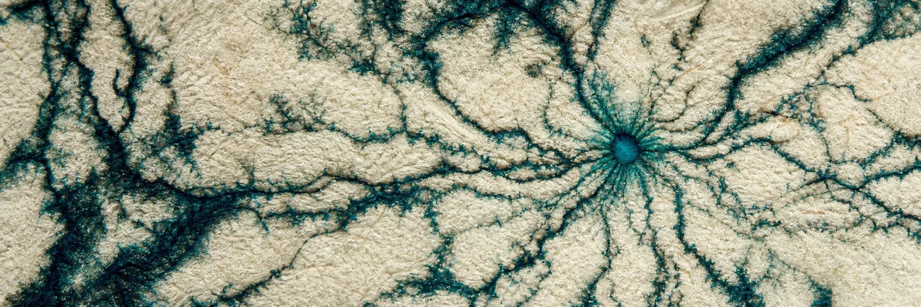 Dark teal ink branching through the fibers of warm handmade paper